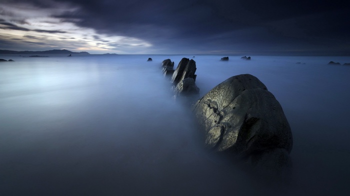 Jagged rocks emerge from misty ocean at dusk