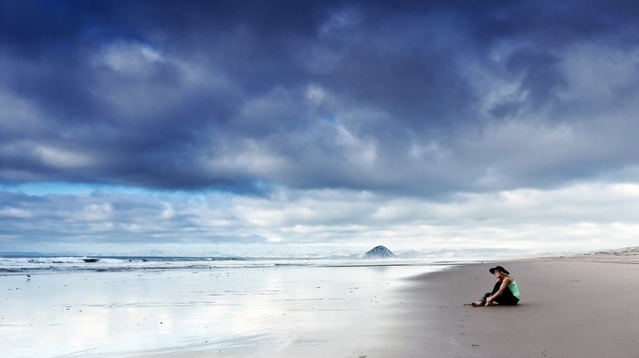 Woman sitting on a beach under stormy clouds