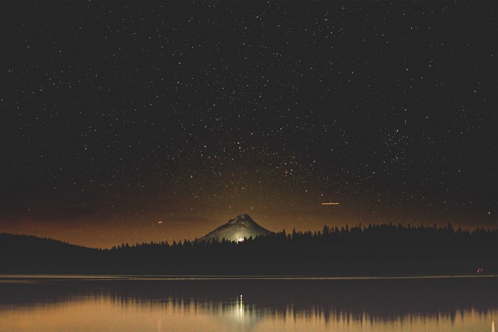 Starry night over a lake with a mountain and forest