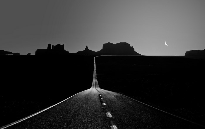 Monochrome road leading to Monument Valley with crescent moon