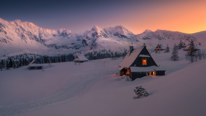 Snowy mountain village at sunset with lit houses