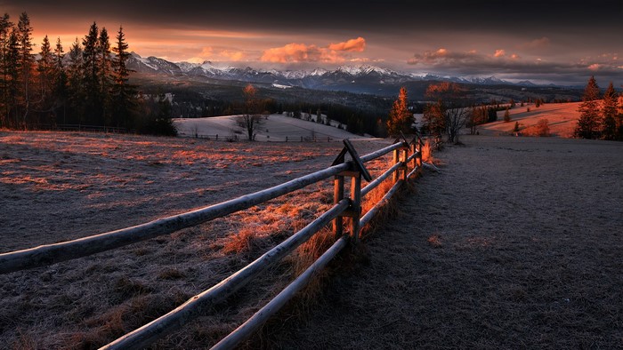 Winter sunset over mountains with wooden fence and frost