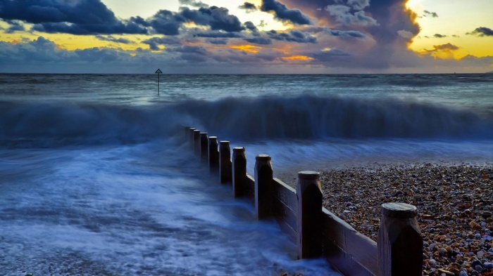 Waves crashing on a pebble beach with a wooden breakwater