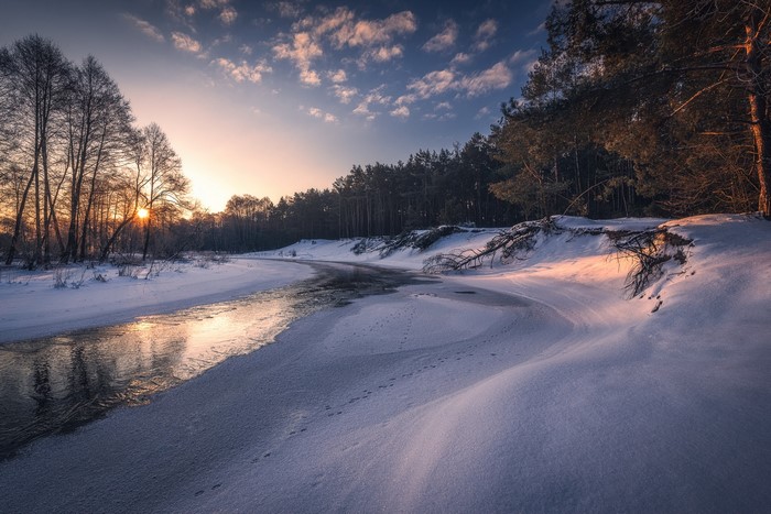 Winter sunset over a frozen river with trees and snow
