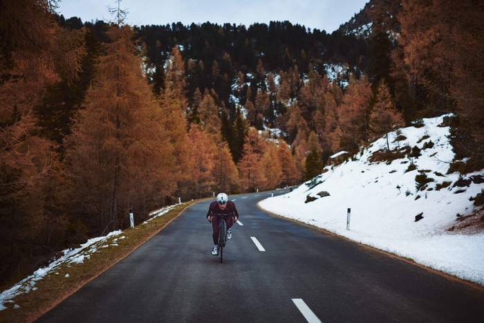 Cyclist on a mountain road with autumn trees and snow