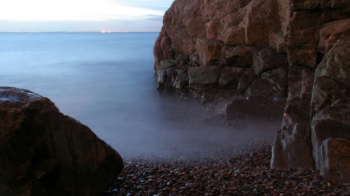 Rocky shore with calm ocean and distant lights