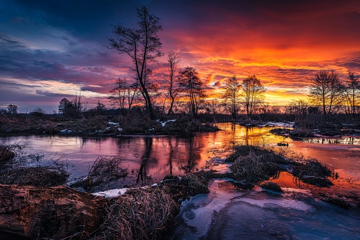 Sunset over a frozen river with trees and clouds