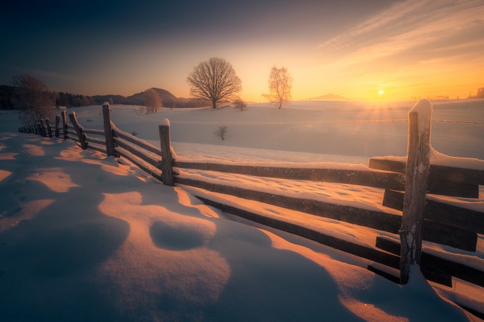 Winter sunset over a snow-covered field with a wooden fence