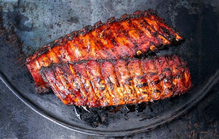 Two racks of barbecued pork ribs on a dark surface