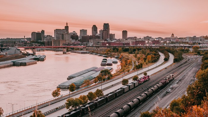 St. Paul skyline with river, barges, and trains at sunset