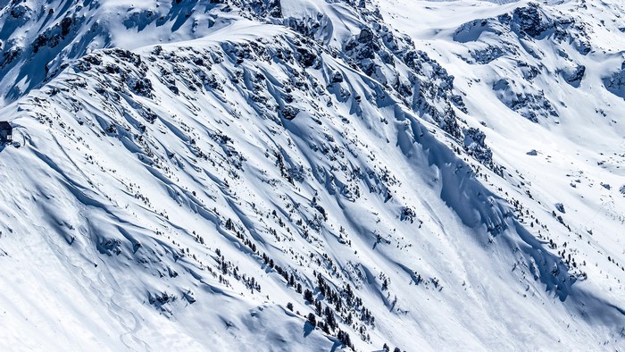 Snowy mountain range with scattered trees and ski tracks