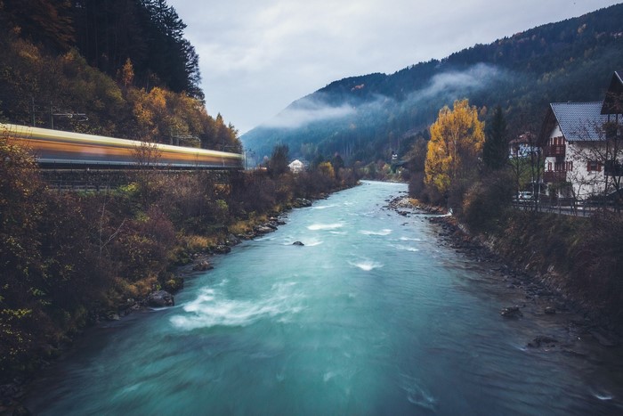 Train passing by a river in a mountainous landscape