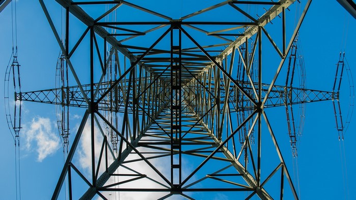 Looking up at a power line tower against a blue sky