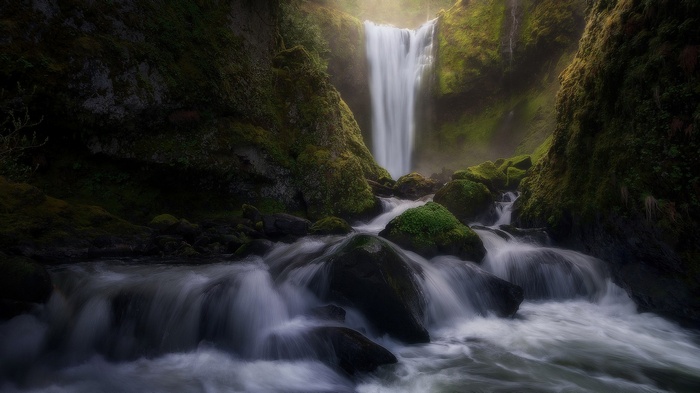 Waterfall cascading over moss-covered rocks in a misty forest