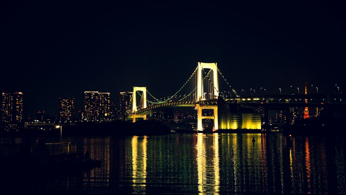 Rainbow Bridge illuminated at night with Tokyo cityscape and water reflection