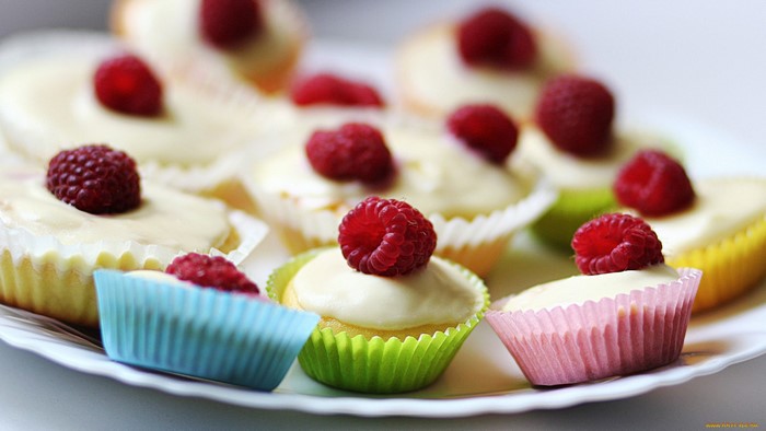 Colorful cupcakes with raspberries on a white plate