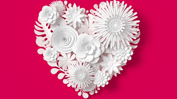 White paper flowers arranged in a heart shape on a pink background