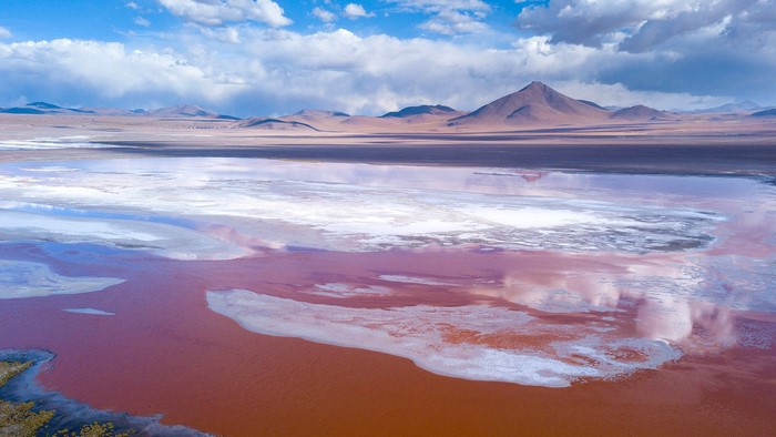 Red and white salt lake with mountains under a cloudy sky