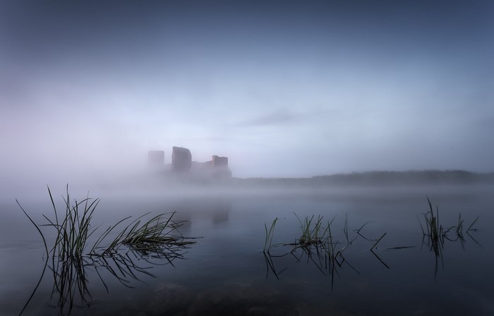 Misty morning over lake with castle ruins