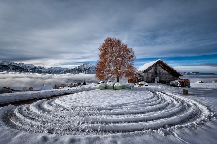 Winter landscape with snow-covered mountains and a barn