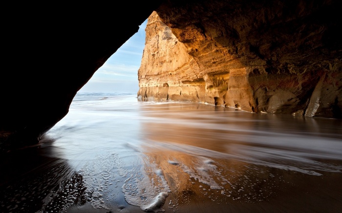 Cave entrance with ocean waves and sandstone cliffs