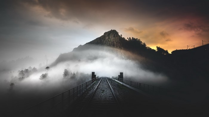 Train tracks through fog towards a mountain at sunset