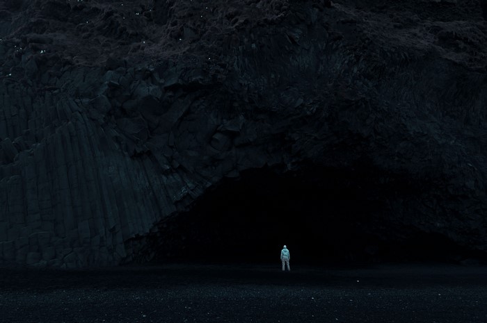 Person in a hazmat suit standing in front of a dark cave entrance