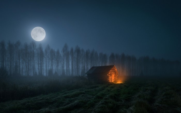 Moonlit night with a glowing shack in a misty field