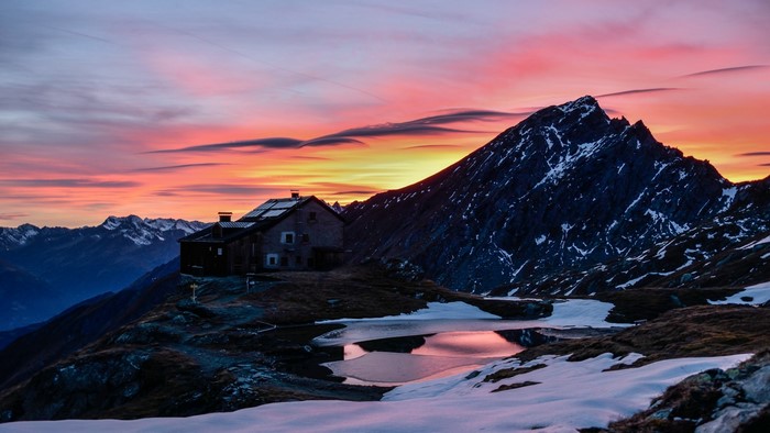 Mountain hut by a lake at sunset with snow