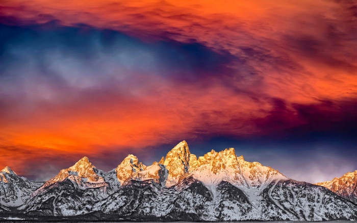 Snow-covered mountains under a fiery sunset sky