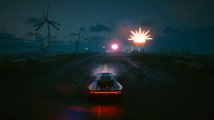 Car driving on a road with wind turbines and neon signs
