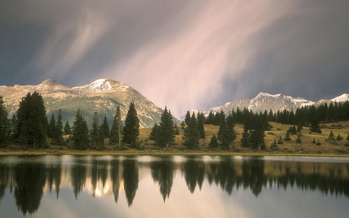 Mountains reflected in a calm lake with pine trees