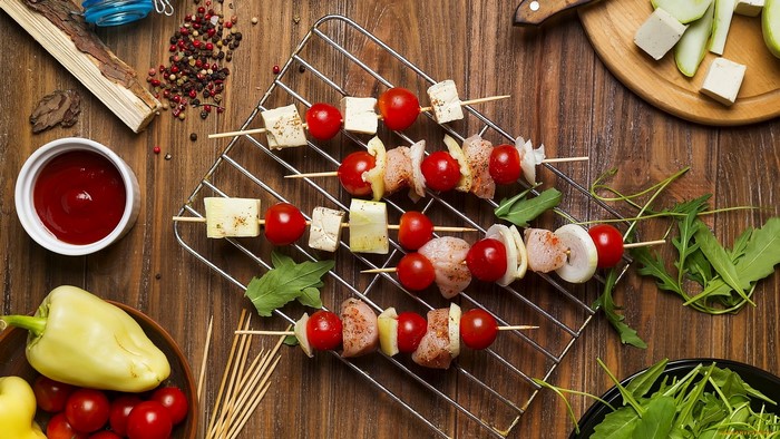Skewers with chicken, tomatoes, cheese, and onions on a grill