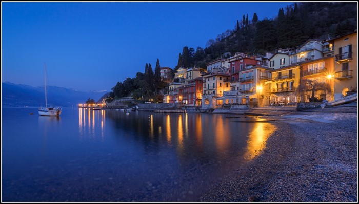 Lake Como at dusk with buildings and a sailboat