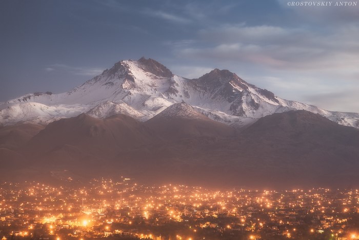Snowy mountain peaks above a glowing city at dusk