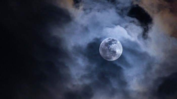 Full moon shining through dark clouds at night
