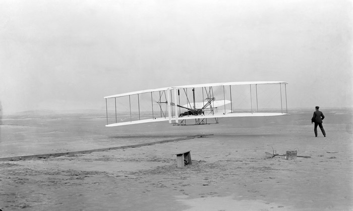Wright Flyer in flight with a man watching