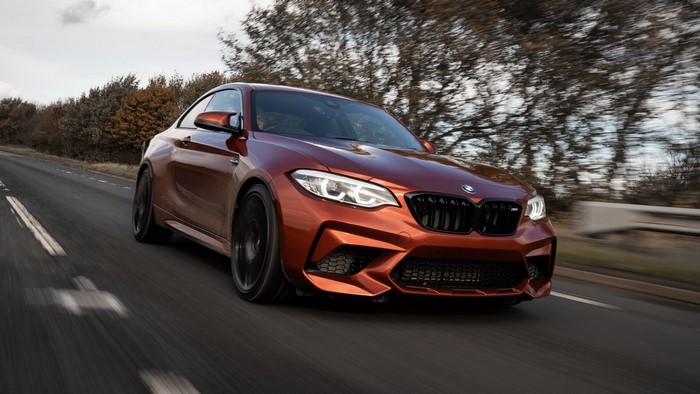 Orange BMW M2 driving on a road with motion blur
