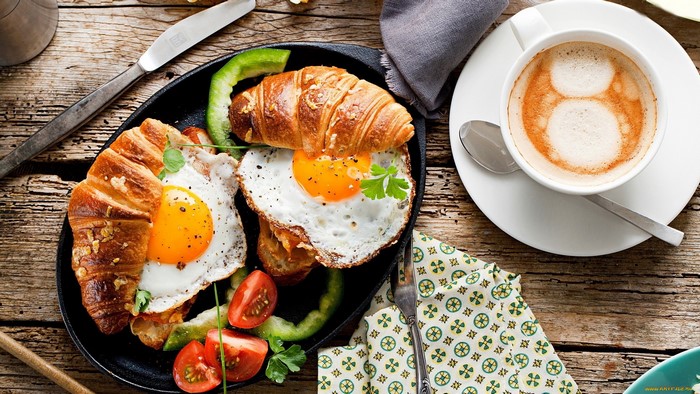 Breakfast with croissants, fried eggs, tomatoes, and coffee