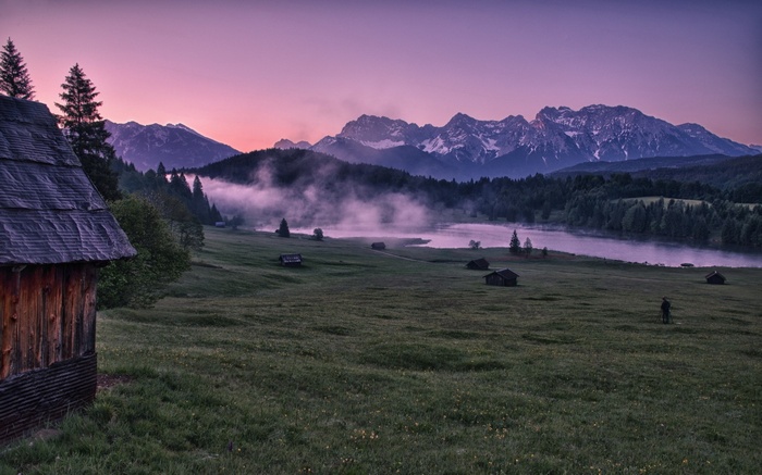 Wooden cabin and misty lake at sunrise with mountains