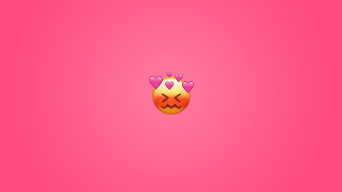 Blushing emoji with hearts on pink background