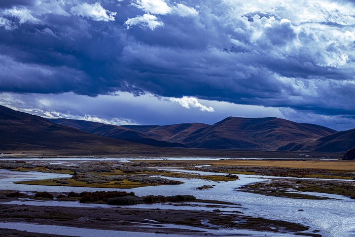 River flowing through a valley with mountains under stormy clouds