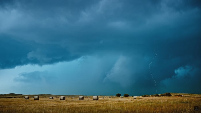 Lightning strikes over a field of hay bales during a storm