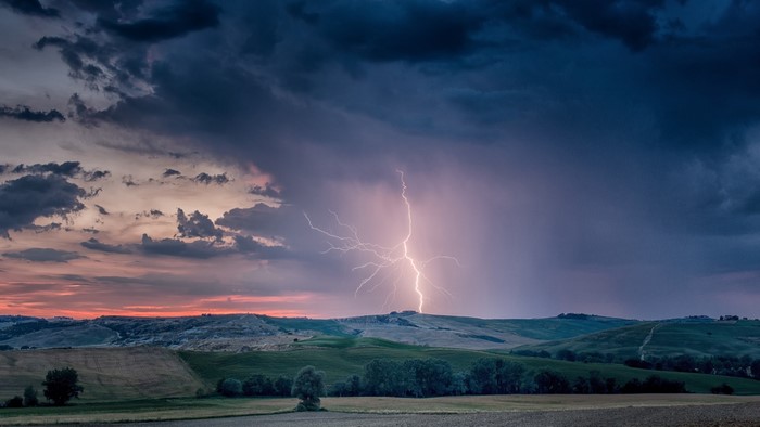 Lightning strikes over rolling hills at sunset