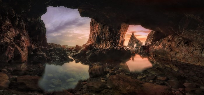 Cave entrance with rock formations and sunset reflection