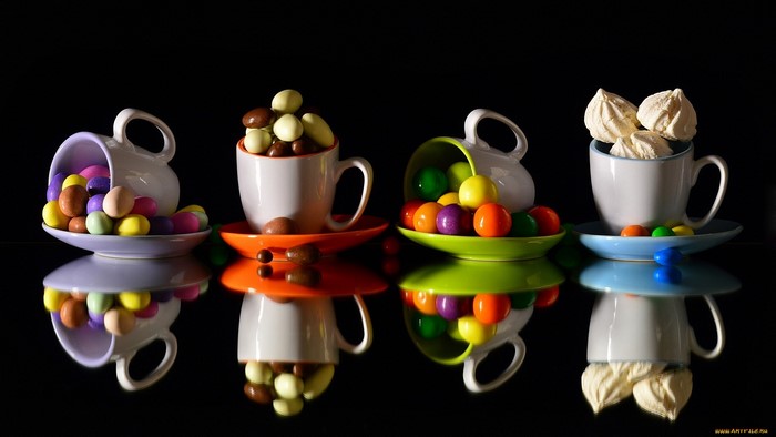 Four cups filled with candy and meringues on a black background