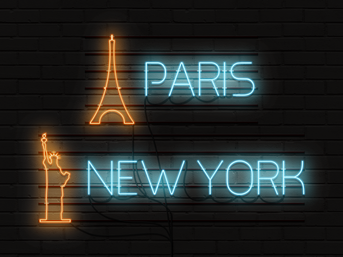 Neon signs of Paris and New York on a brick wall