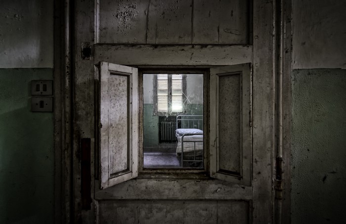 Abandoned room with a bed seen through a doorway