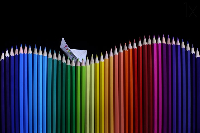 Colored pencils arranged in a wave with a paper boat