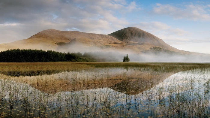Misty mountains reflected in a calm lake with reeds